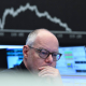 03 April 2025, Hesse, Frankfurt/Main: A stock market trader watches his monitors on the trading floor of the Frankfurt Stock Exchange as the display board with the DAX curve shows falling prices.  Arne Dedert/dpa