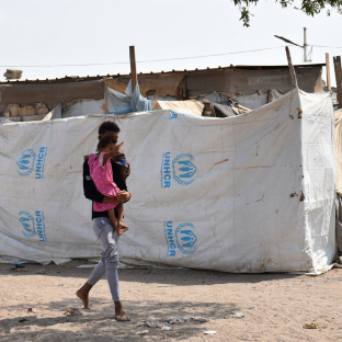 Un hombre desplazado, con su hijo en brazos, camina junto a unas tiendas de campaña en un campamento provisional para desplazados a las afueras de Adén (Yemen) Murad / Xinhua News / Europa Press