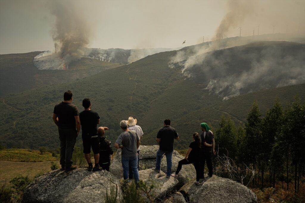Varias personas ven cómo los efectivos aéreos trabajan en la extinción del incendio de Avión (Ourense). Adrián Irago/Europa Press.