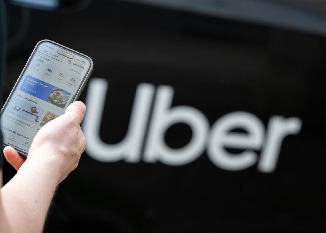 Archivo - FILED - 08 August 2024, Berlin: A man stands in front of a rental car with a sign from the mobility service provider and ride broker Uber and holds his smartphone with the company's app in his hand. Photo: Sebastian Gollnow/dpaSebastian Gollnow/dpa - Archivo