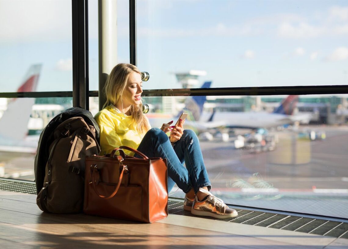 Archivo - Woman sitting in airport and waiting for her flight, woman using phone in airport departure areaGRINVALDS - Archivo