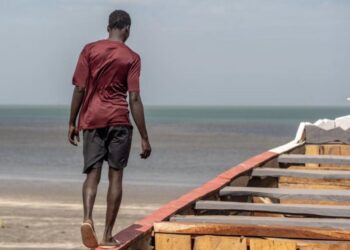 Un hombre camina sobre una barca en la costa de GambiaOIM/LAMIN SANNEH