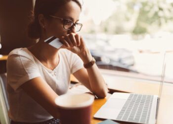 Mujer delante de un ordenador portátil con una tarjeta bancaria en la manoSAS