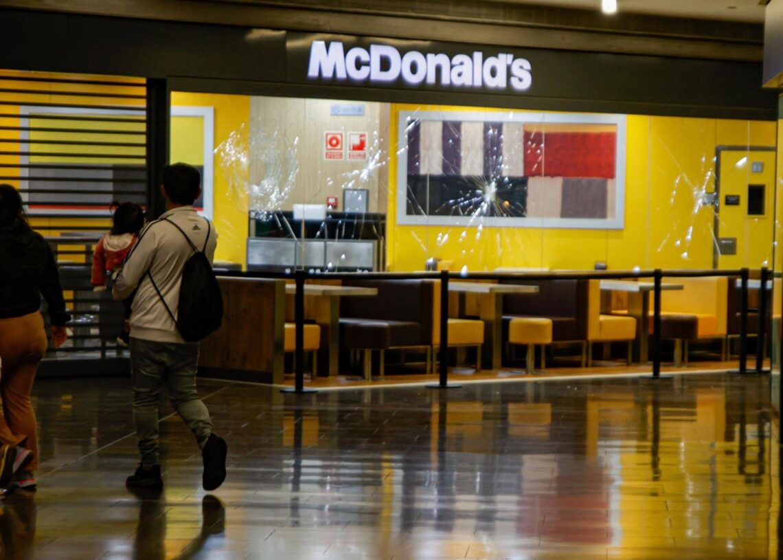 Archivo - Dos personas pasan delante del escaparate del McDonald's con los cristales rotos en el centro comercial Màgic Badalona, a 27 de marzo de 2024, en Badalona, Catalunya (España). Kike Rincón - Europa Press - Archivo